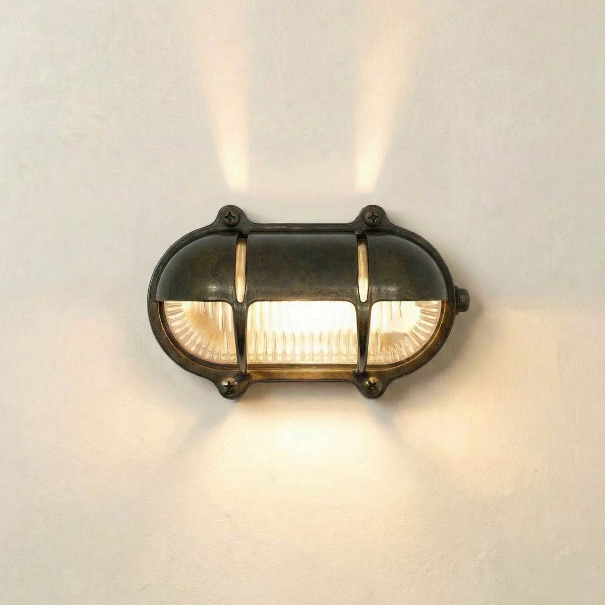 Oval eyelid bulkhead light with uplight in solid antique brass and rated IP64, shown lit.