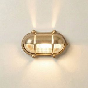 Oval eyelid bulkhead light with uplight in solid raw brass and rated IP64, shown lit.
