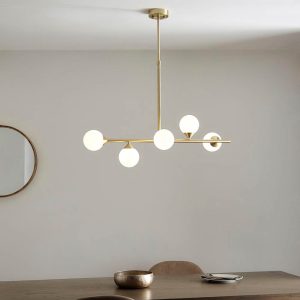 Modern 5 light pendant bar in satin brass with opal glass shades, shown over a dining room table.