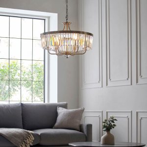 Round 6 light chandelier in antique brass with cut glass drops, shown in a lounge setting.