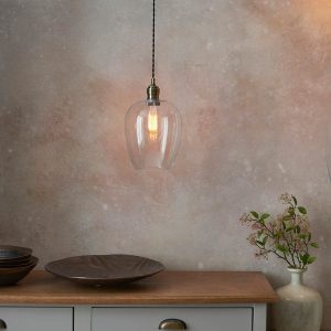 Small clear glass kitchen pendant in antique brass, shown over a dining room sideboard.