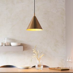 Classic single light metal kitchen pendant in antique brass with cone-shaped shade, shown over a dining table.