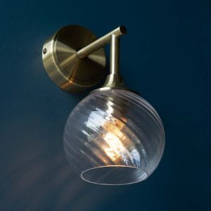 Allegra antique brass wall light with twisted clear glass shade on dark blue wall