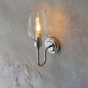 Classic polished nickel wall light with clear glass shade, shown on room wall.