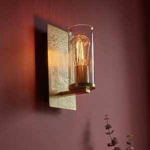 Hammered handmade industrial wall light in plated brass, shown on burgundy wall.