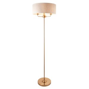 Highclere 3 light floor lamp standard in vintage brass with natural linen shade, on white background, lit.