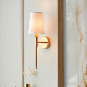 Traditional vintage brass single wall light with vintage white shade, shown on living room wall.