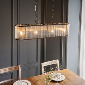 Ridgeton 4 light linear pendant in antique brass with clear ribbed glass shade, shown over a dining room table.