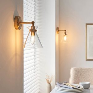 Harlow single wall light in aged brass with adjustable clear glass shade, on dining room wall.
