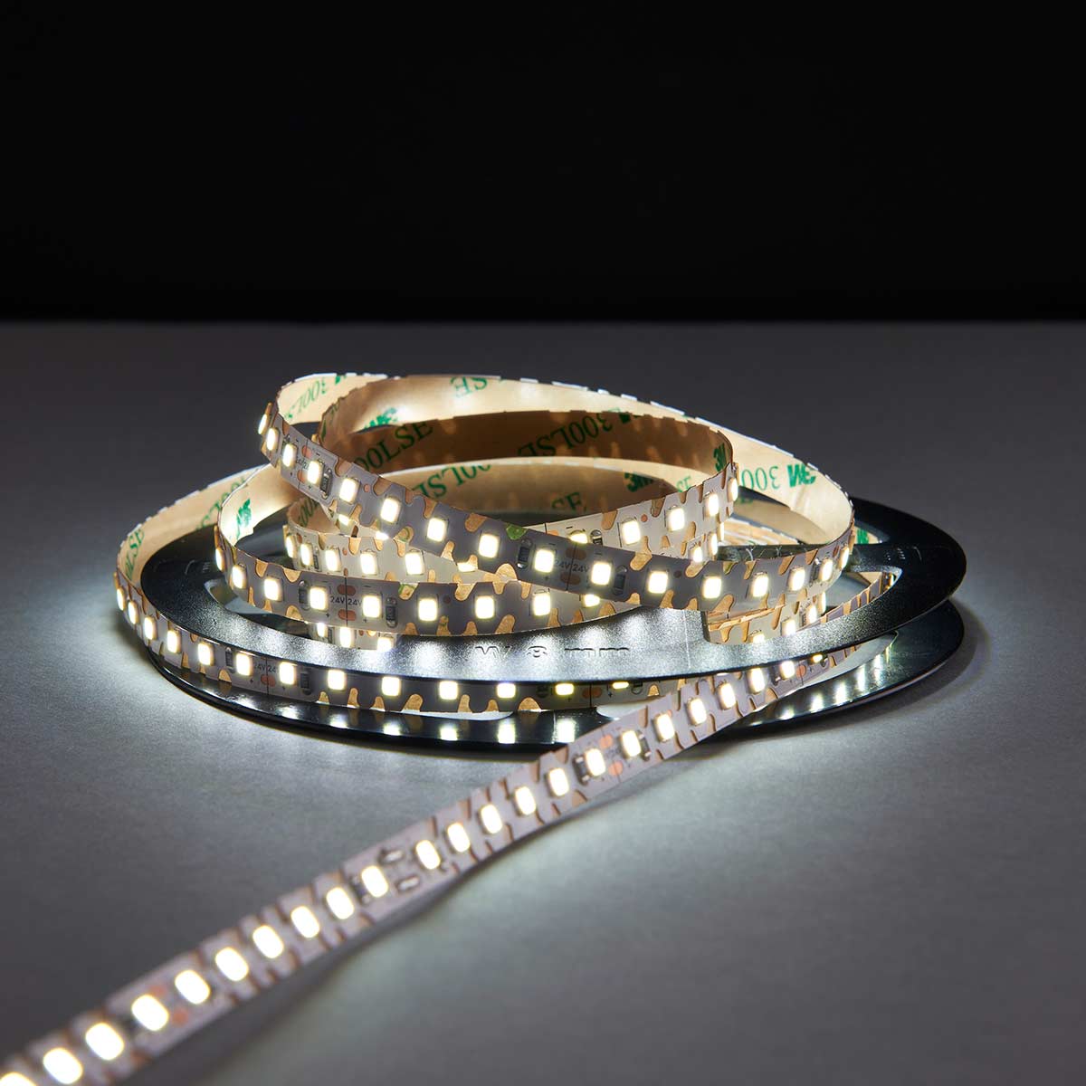 OrionFLEX 24V daylight white self-adhesive LED tape in 5m roll, shown lit on roll, with dark background.
