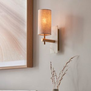 White marble wall light in vintage brass with natural linen cylinder shade, shown facing up on a room wall.