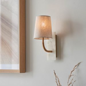Curved arm wall light with white marble fascia and tapered shade in vintage brass, shown on room wall.