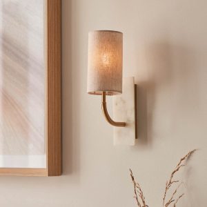 Curved arm wall light with white marble fascia and cylinder shade in vintage brass, shown on room wall.
