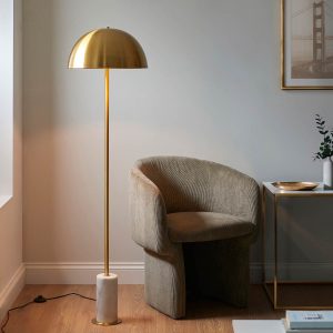 Aged brass designer floor lamp with white marble base and mushroom shade, shown in a lounge setting.