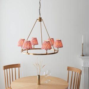 Round aged brass 5 light chandelier with pink Ikat shades, shown lit over a dining room table.