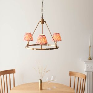Round aged brass 3 light chandelier with pink Ikat shades, shown lit over a dining room table.