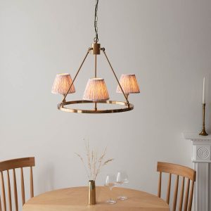 Round aged brass 3 light chandelier with peach leaf shades, lit over a dining room table.
