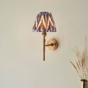 Single aged brass wall light with grey zigzag shade, shown on room wall.