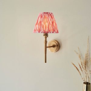Single aged brass wall light with coral pink Ikat shade, shown on room wall.