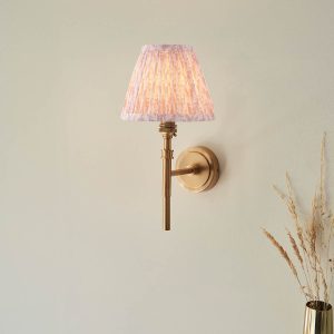 Single aged brass wall light with peach leaf shade, shown on room wall.