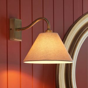 Knole classic antique brass wall light with natural faux linen shade, angled view on salmon panelled wall.