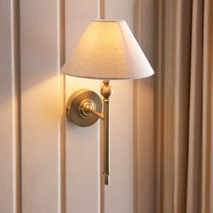 Lille antique brass single wall light with natural faux linen shade, shown on panelled wall.