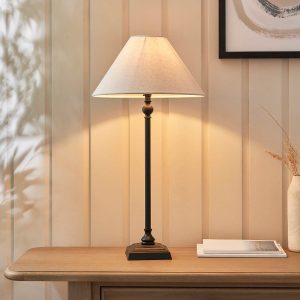 Lille candlestick table lamp in matt black with natural faux linen shade, shown on living room side table.