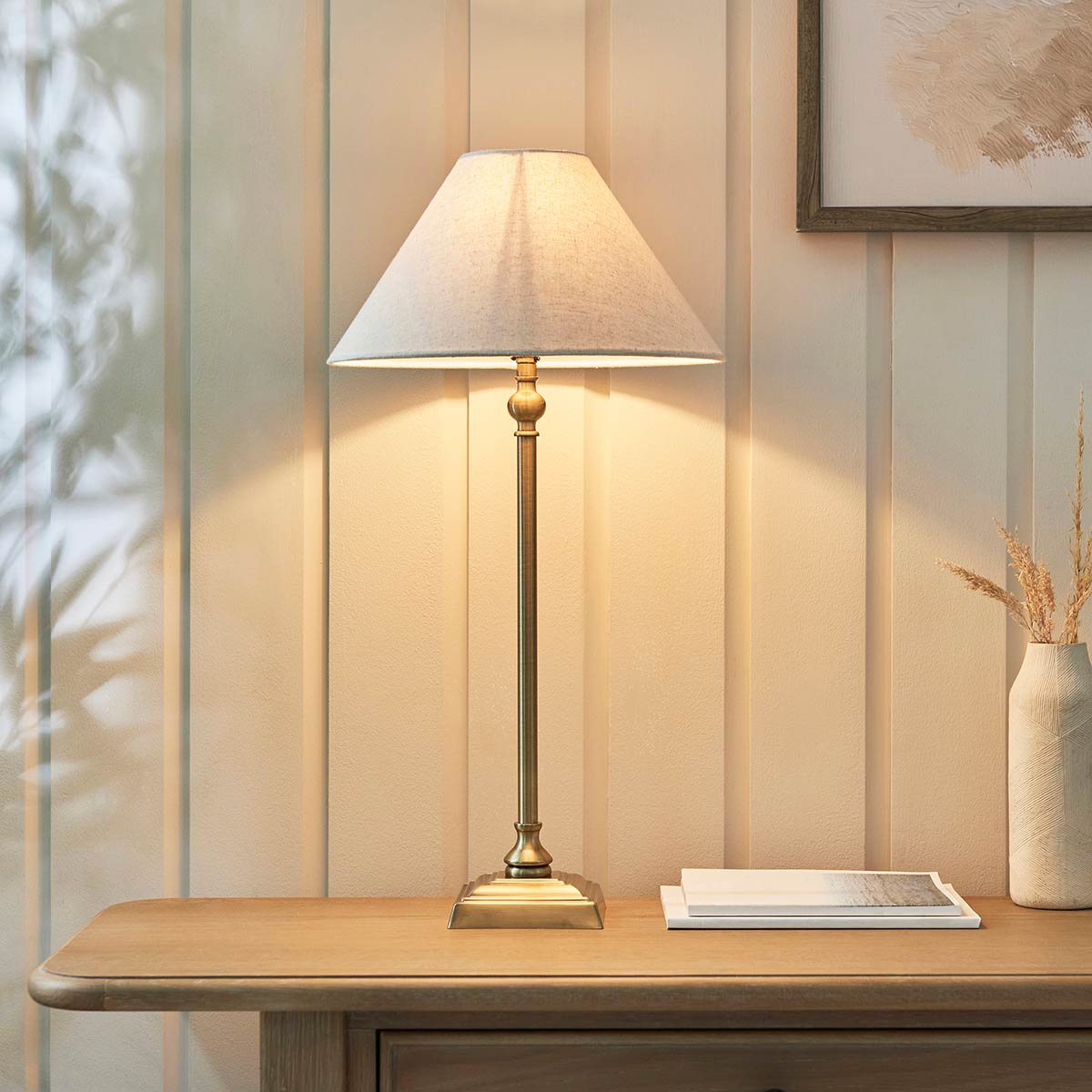 Lille antique brass candlestick table lamp with natural faux linen shade, shown on lounge side table.