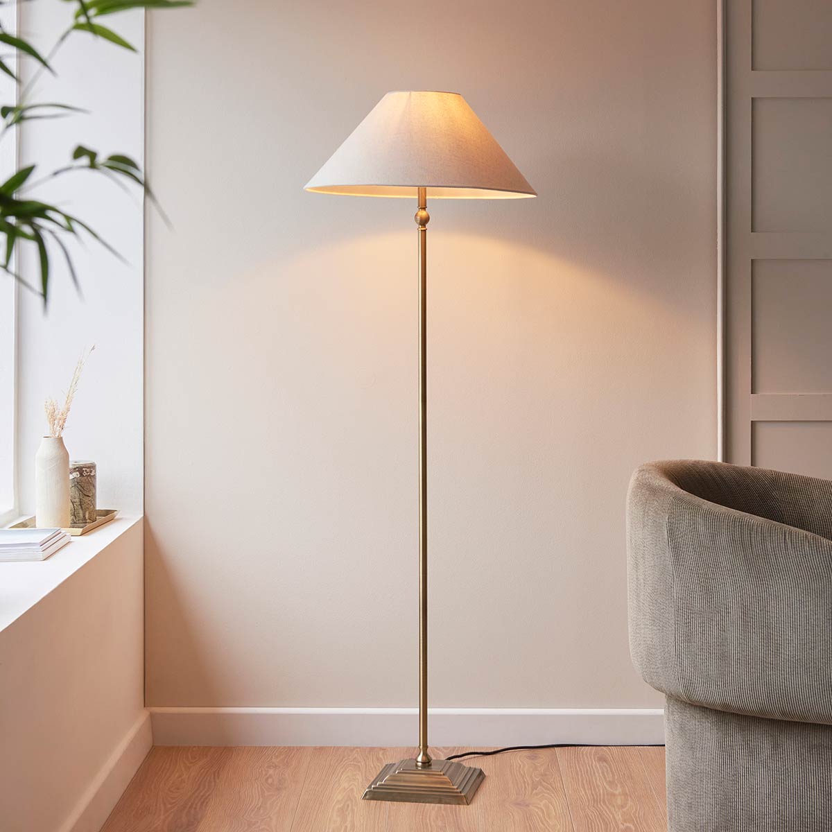 Lille antique brass candlestick floor lamp with natural faux linen shade, shown in lounge setting.