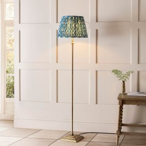 Lille antique brass candlestick floor lamp with blue Ikat shade, shown in a living room setting.