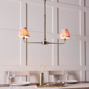 Lille linear 2 light antique brass pendant with pink Ikat shades, shown over a dining room table.