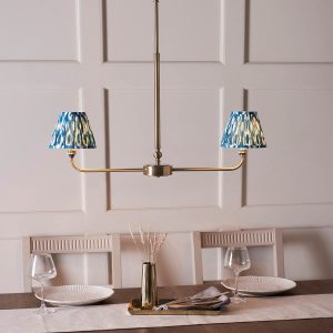 Lille linear 2 light antique brass pendant with blue Ikat shades, shown over a dining room table.