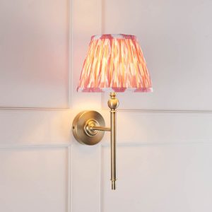 Lille single antique brass wall light with pink Ikat shade, angled view in panelled room.