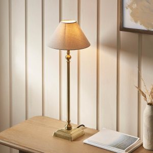 Lille small antique brass candlestick table lamp with natural faux linen shade, shown on sitting room side table.