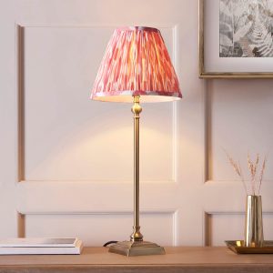 Lille antique brass candlestick table lamp with pink Ikat shade, shown on a living room sideboard.