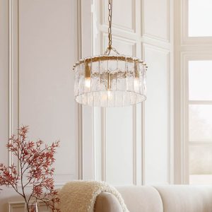 Karine 3 light pendant in brushed aged brass with textured handmade glass, shown over sofa in a lounge setting.