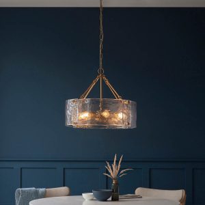 Keller 6 light pendant in aged brass with textured handmade glass, shown hanging over a dining room table.