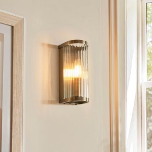 Ridgeton 1 light wall light in antique brass with clear ribbed glass shade, shown in room setting.