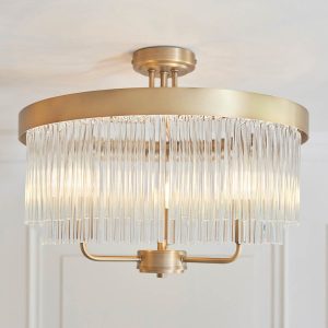Clermont 3 light semi flush ceiling light in antique brass with clear glass rods, shown in room setting.