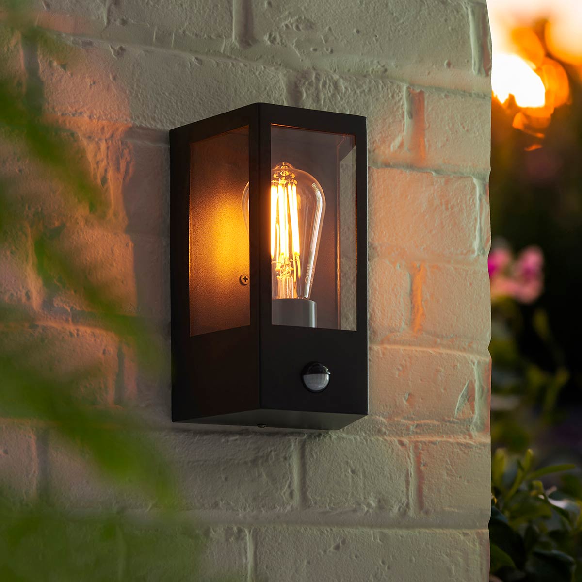 Huntington PIR wall box lantern in matt black with clear ribbed glass and rated IP44, shown on external brick wall.