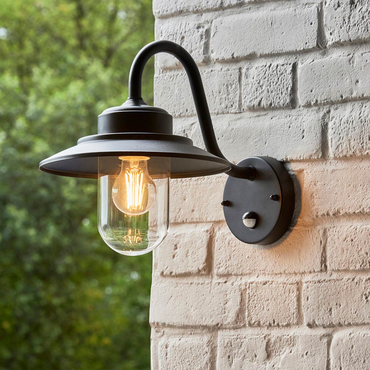 Thornton traditional PIR wall lantern in matt black with clear pill glass shade and rated IP44, shown on exterior brick wall.