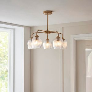 Ashcroft 5 light pendant in brushed aged brass with clear ribbed glass goblet shades, shown in room setting.