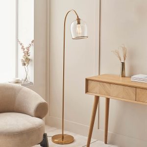 Ashcroft floor lamp in brushed aged brass with clear glass goblet shade, shown in a lounge setting.