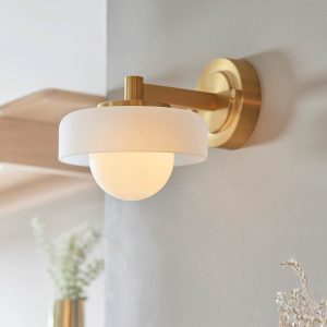 Boss single wall light in brushed aged brass, shown on living room wall.