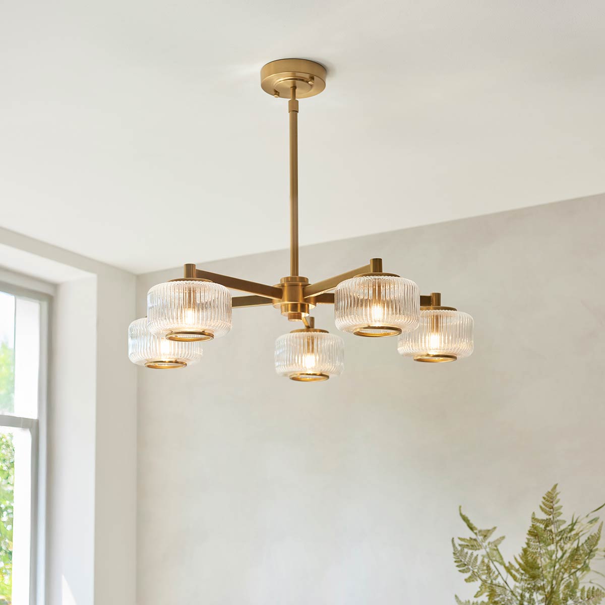 Stamford 5 light pendant in brushed aged brass with clear ribbed glass drum shades, shown in a room setting.