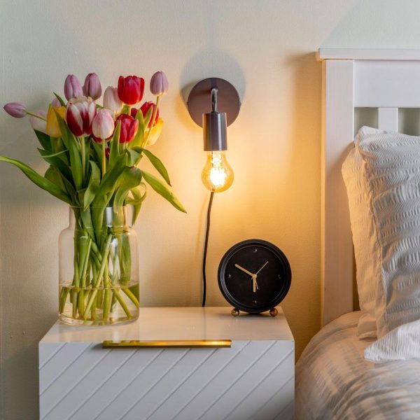 Plug in wall light in charcoal, shown lit on bedroom wall