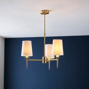 Traditional 3 light chandelier in satin brass with vintage white shades, shown in a blue room.