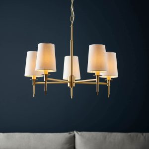 Traditional 5 light chandelier in satin brass with vintage white shades, shown in sitting room.