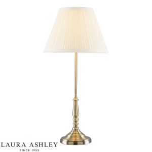 Elliot candlestick table lamp in antique brass finish with ivory shade by Laura Ashley, on white background, lit.
