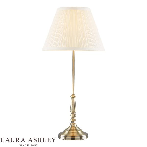 Elliot candlestick table lamp in antique brass finish with ivory shade by Laura Ashley, on white background, lit.